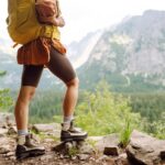 Turista s veľkým batohom stojí na vrchole hory a obdivuje panoramatický výhľad na horskú krajinu.